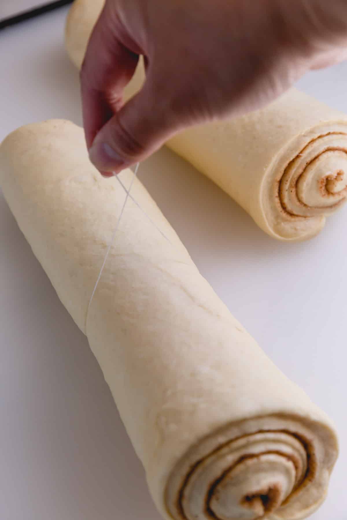 Two rolls of caramel rolls, one being sliced with dental floss.