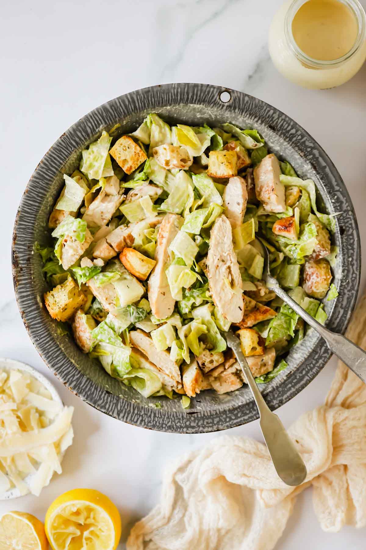 Overhead image of a bowl of chicken Caesar salad with serving spoons sticking out.