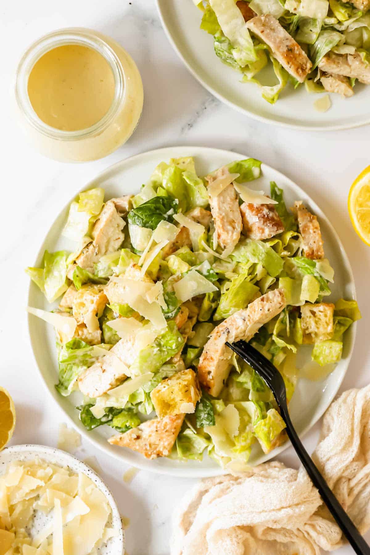 A plate of chicken Caesar salad with a fork spearing a piece of chicken and dressing on the side.