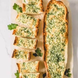 Two loaves of garlic bread topped with an herbed butter spread with one sliced into pieces.
