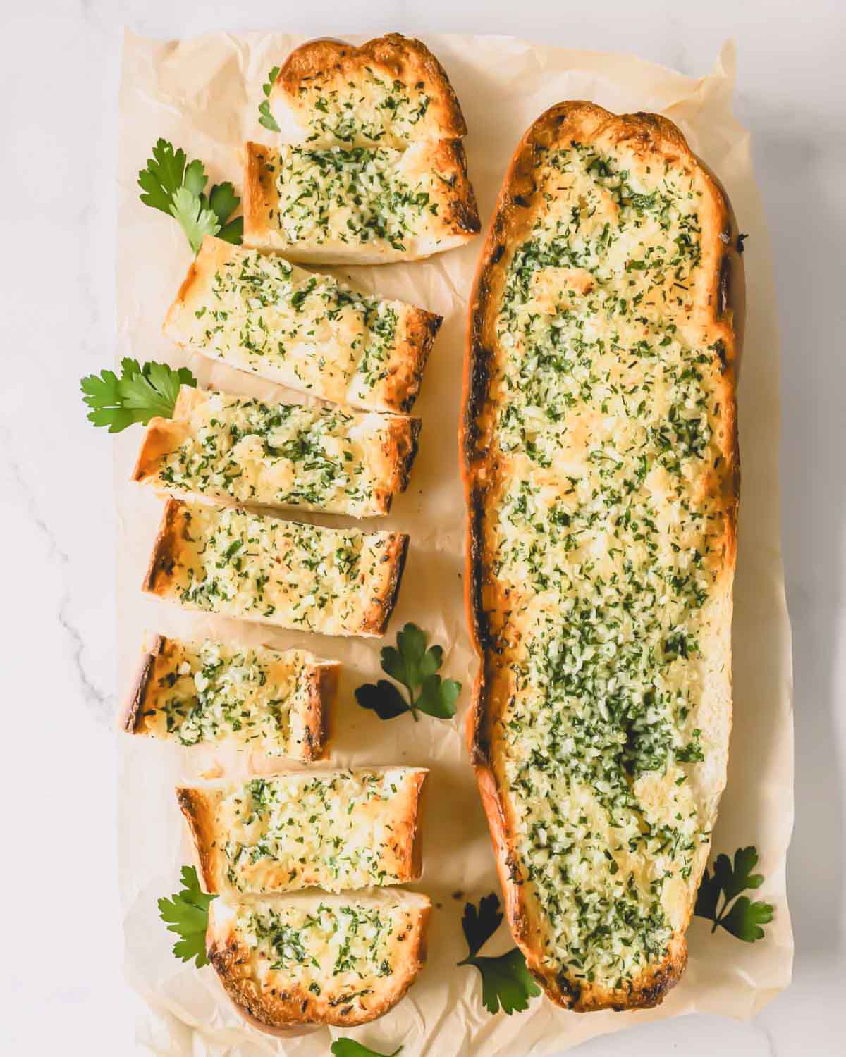 Two loaves of garlic bread topped with an herbed butter spread with one sliced into pieces.