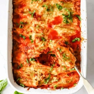 A dish of pesto ricotta stuffed pasta shells with a spoon scooping up a shell.