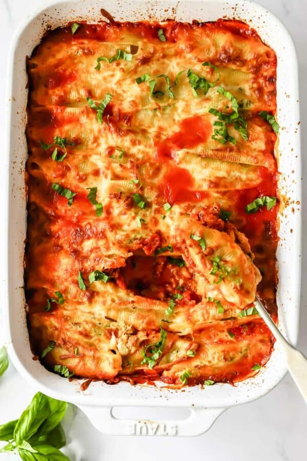A dish of pesto ricotta stuffed pasta shells with a spoon scooping up a shell.