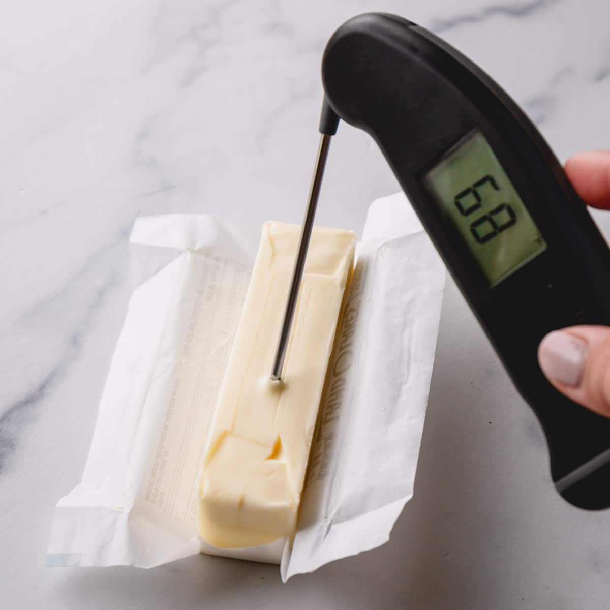 A stick of butter with inserted instant thermometer at 68°F.