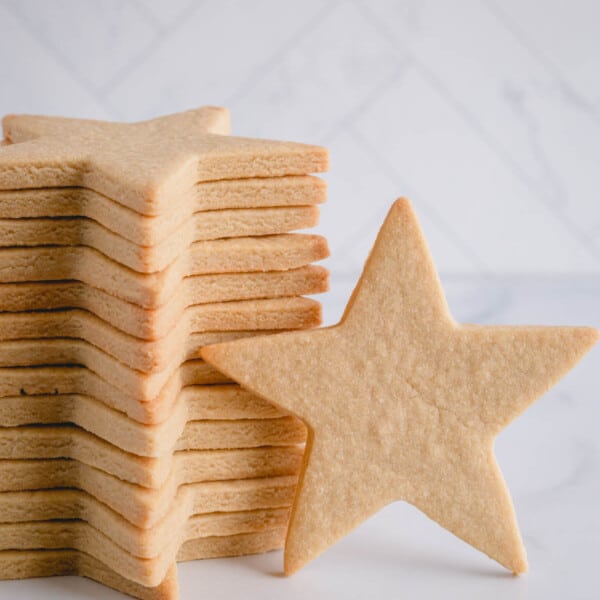 One large star shaped sugar cookie standing against a stacked cookies.