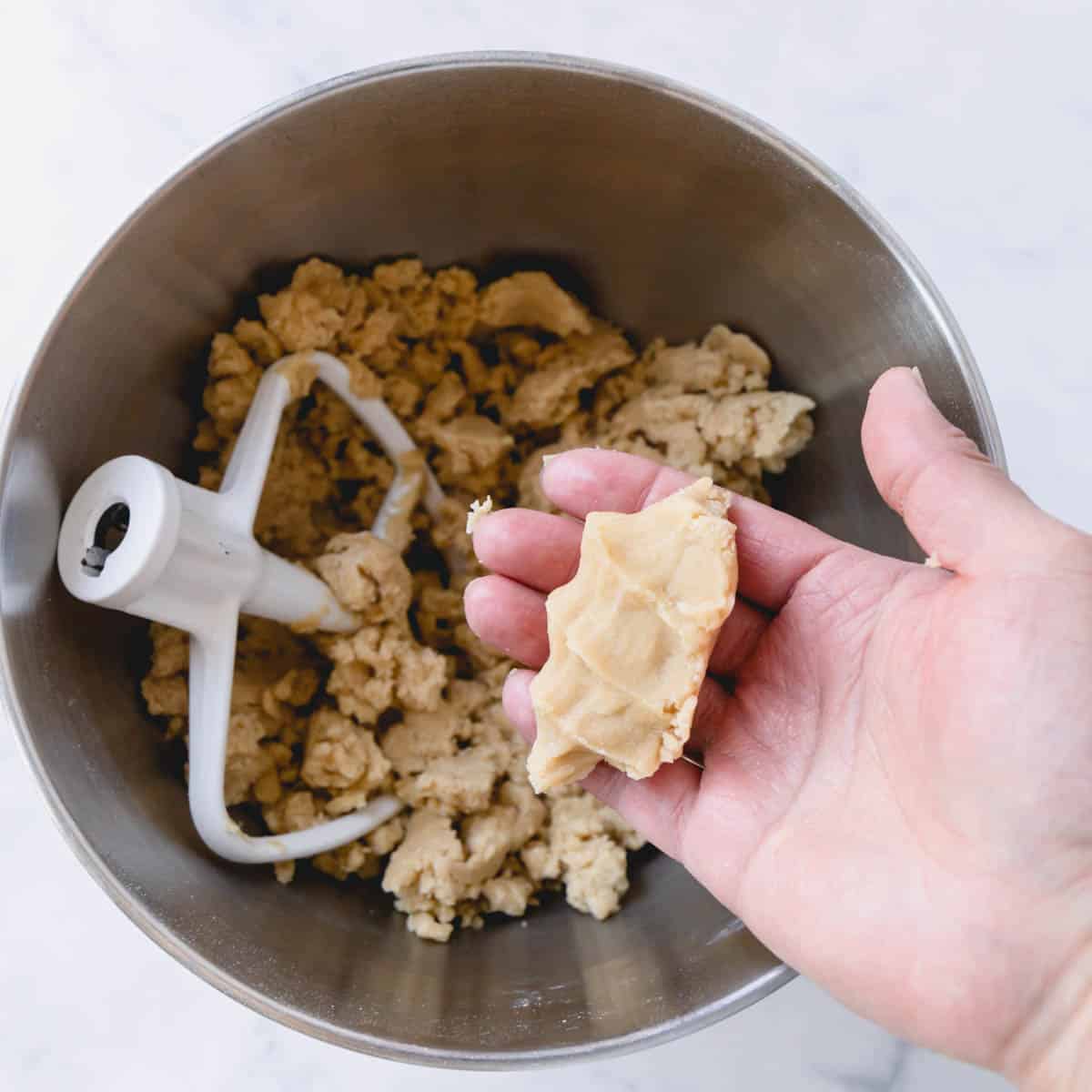Crumbly cookie dough in a mixing bowl and some squeezed in hand.