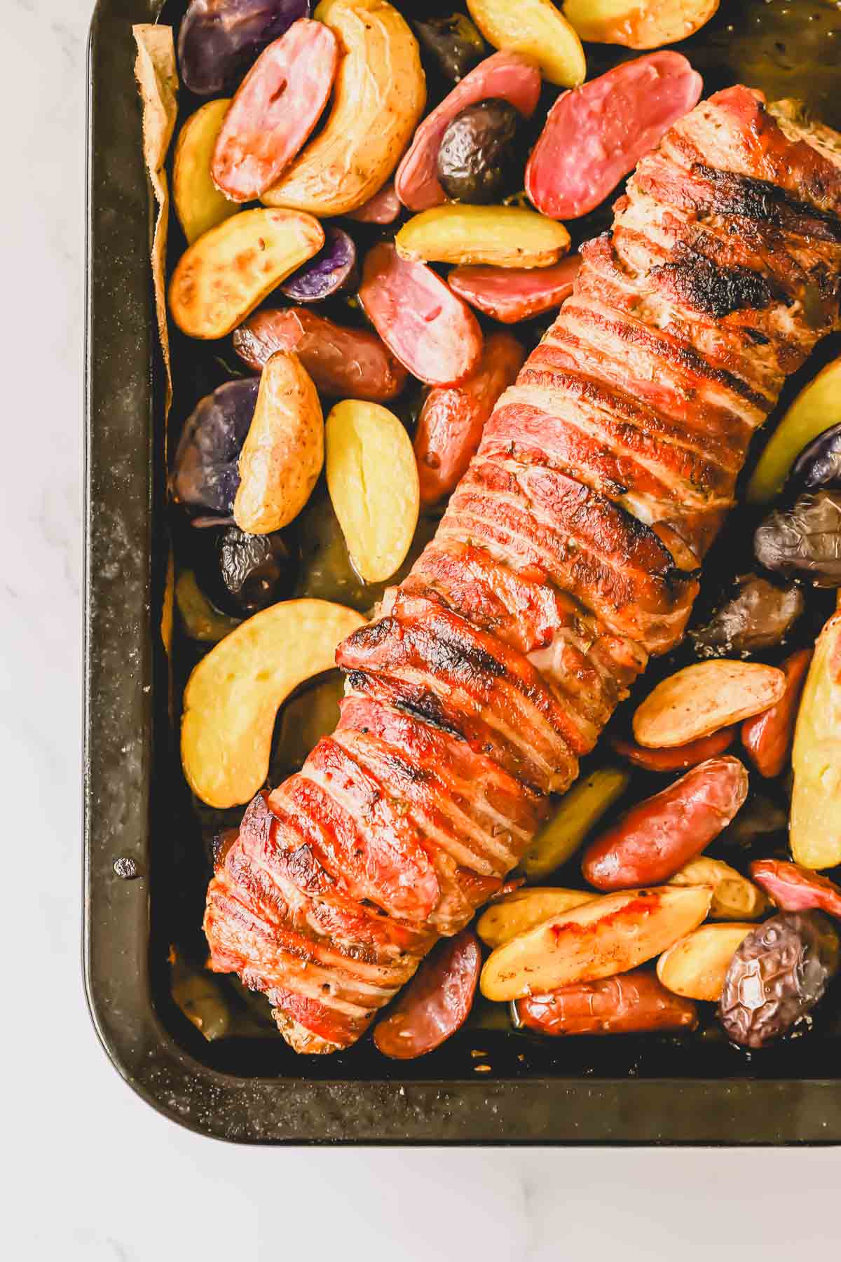 A baking tray with potatoes and a full bacon wrapped tenderloin.