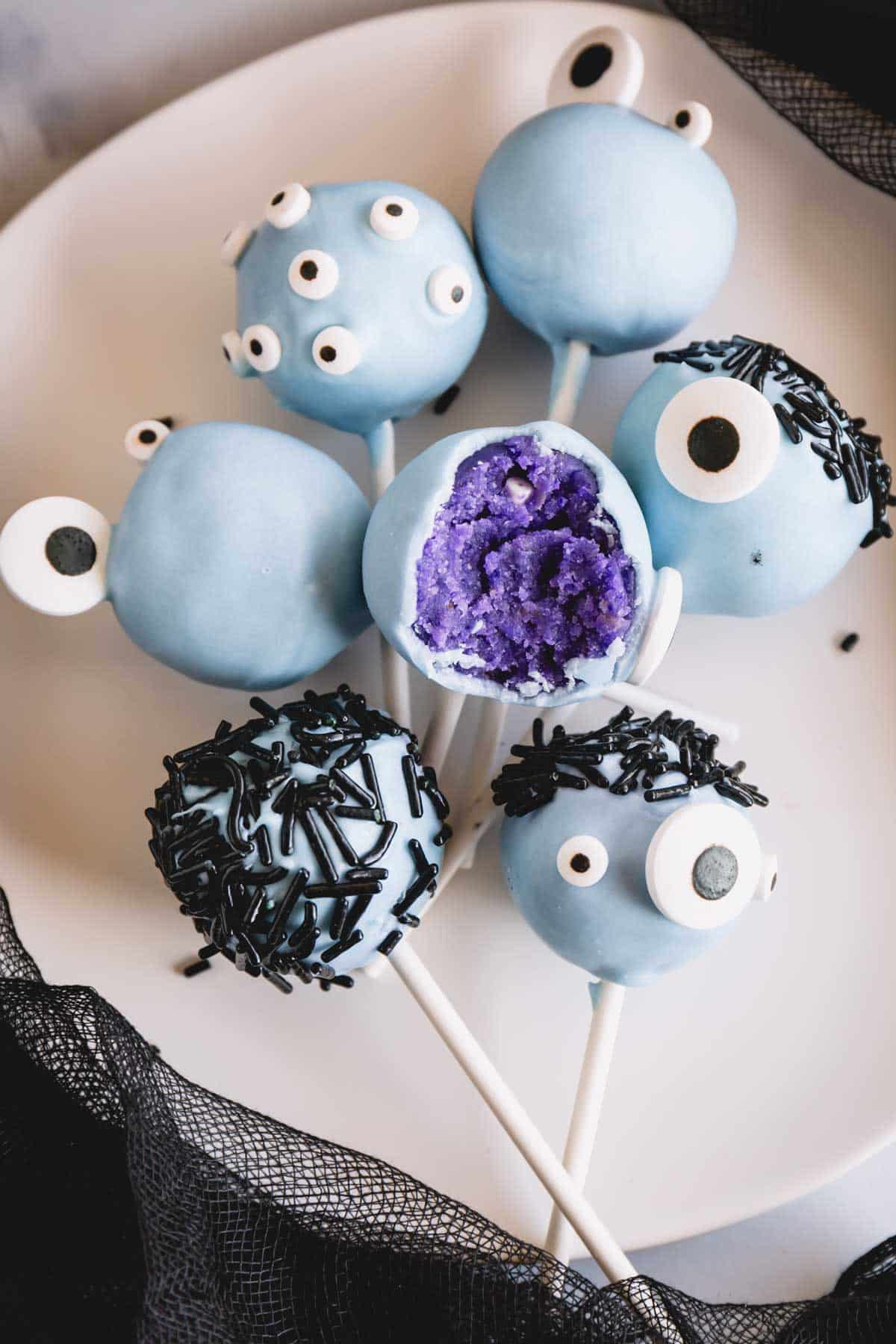 Blue monster cake pops with candy eyes and sprinkle hair with a bite missing from one.