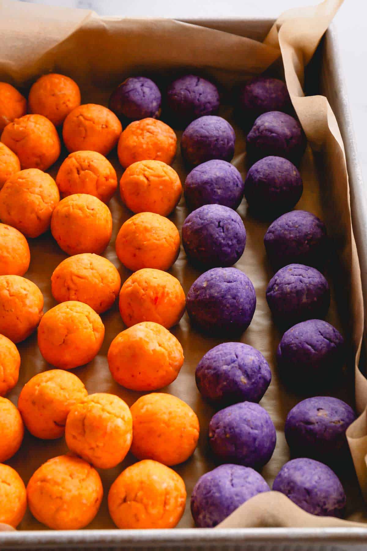 Orange and purple cake pop balls on top of parchment paper in a tray.