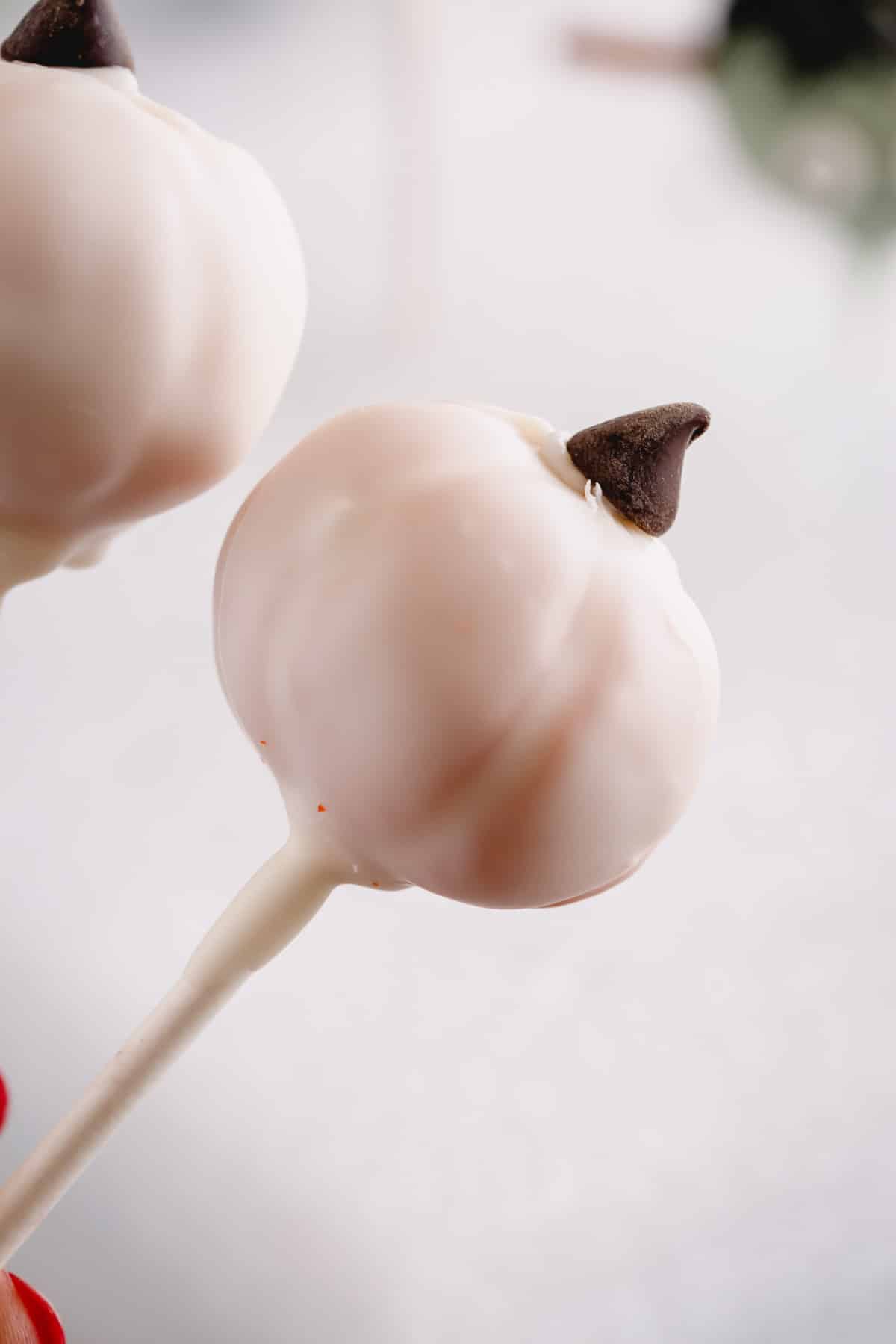 A white pumpkin cake pop topped with a mini chocolate chip.