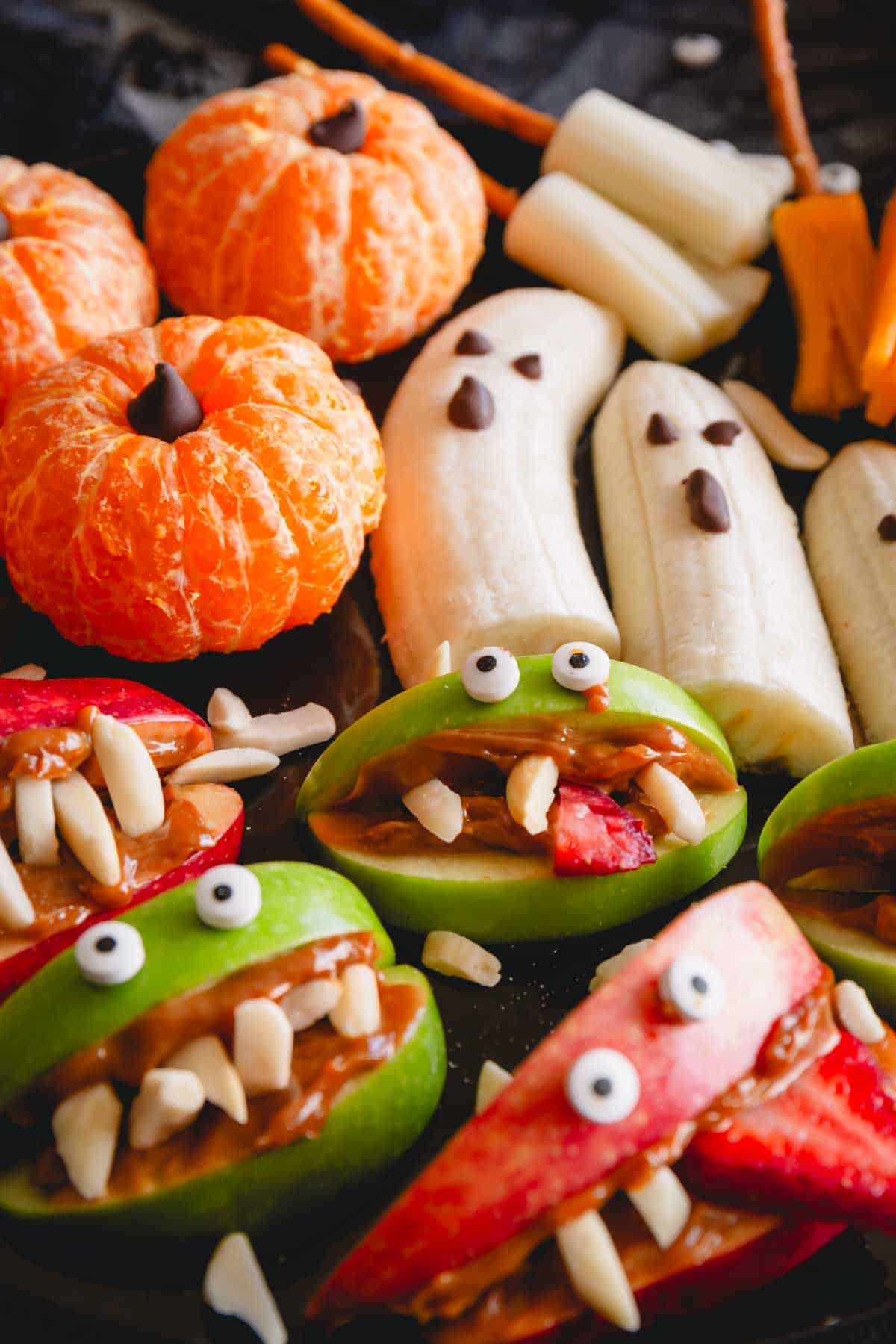 Pumpkin oranges, banana ghosts, and monster apples on a Halloween snack board.