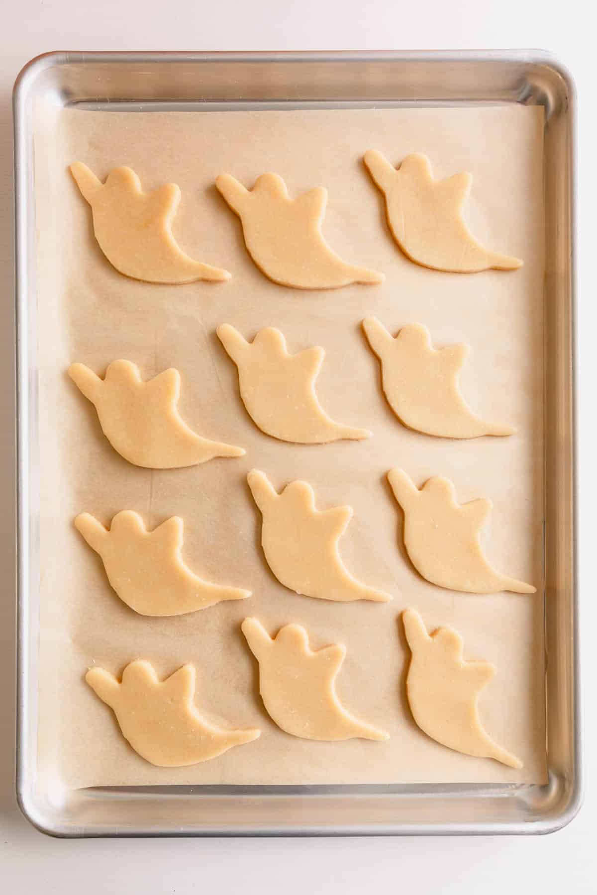 Unbaked ghost cutout cookies on a baking sheet.
