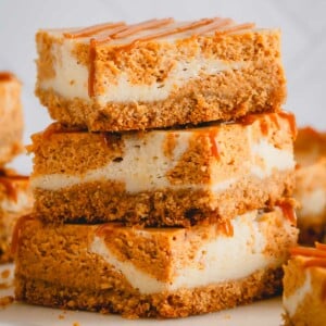A stack of three pumpkin cheesecake bars with graham cracker crust.