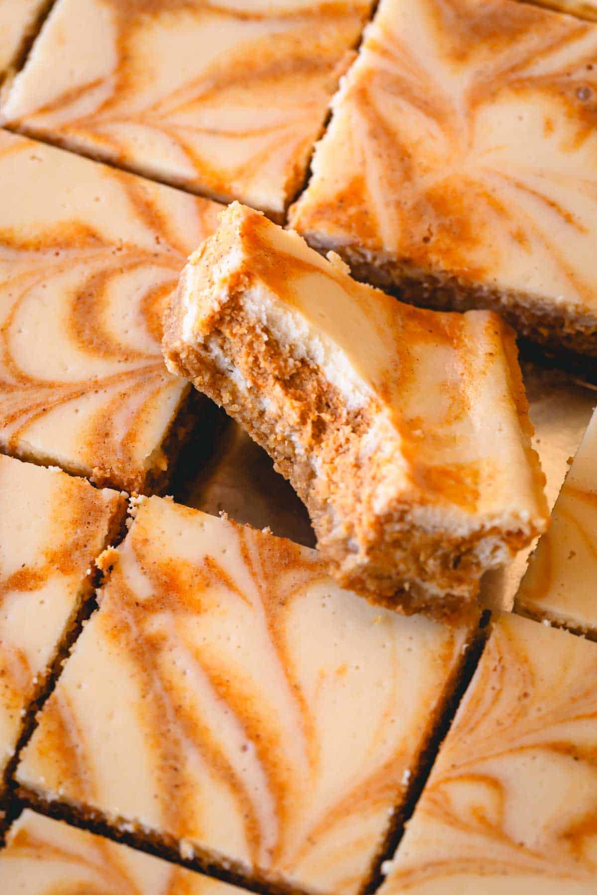 Close up image of squares of pumpkin cheesecake bars with one missing a bite.