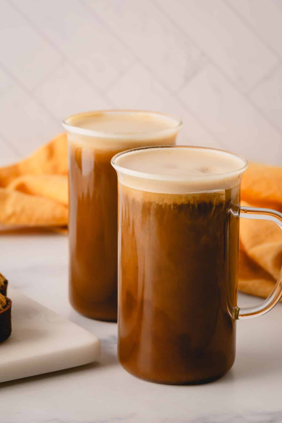 Two glass mugs full of coffee topped with pumpkin mousse.