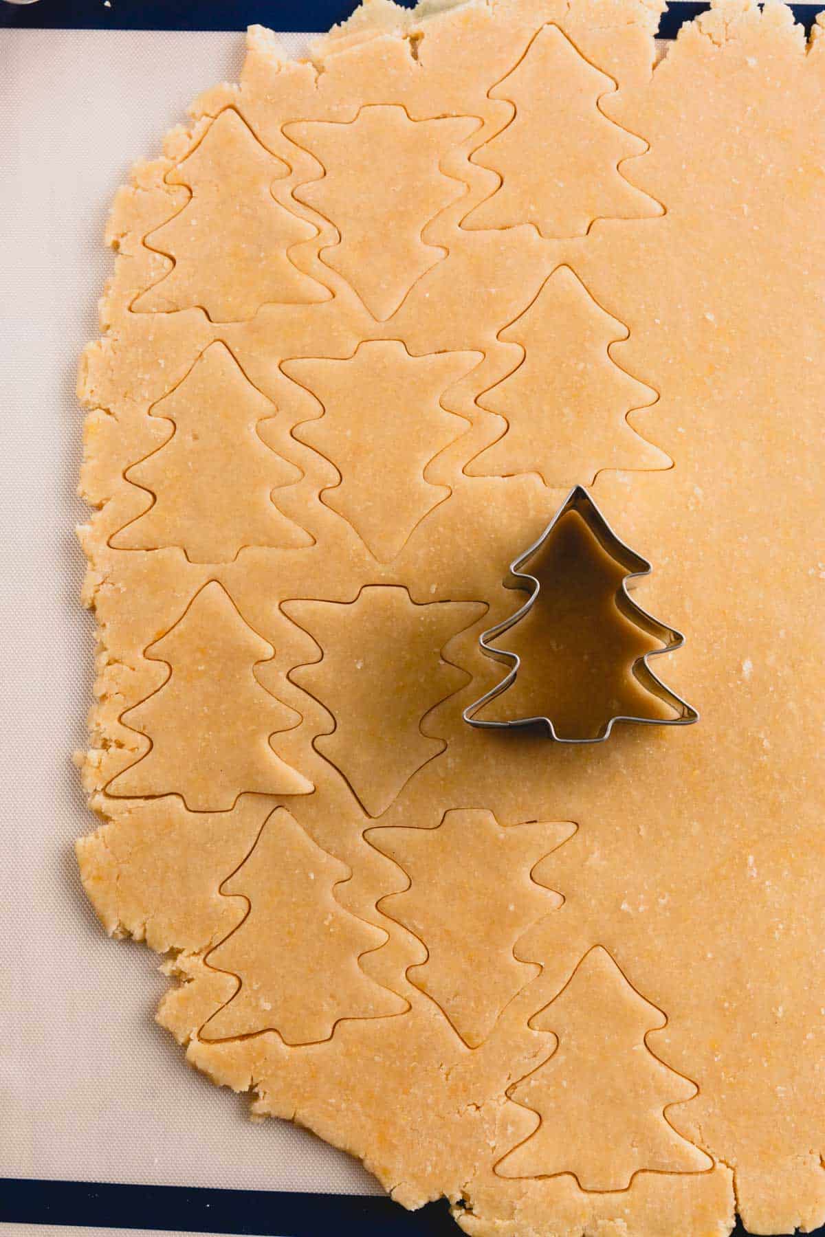 Sugar cookie dough being cut with a Christmas tree cookie cutter.