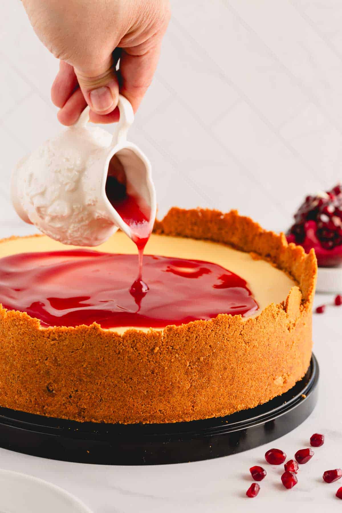 Pomegranate sauce being poured over cheesecake filling.