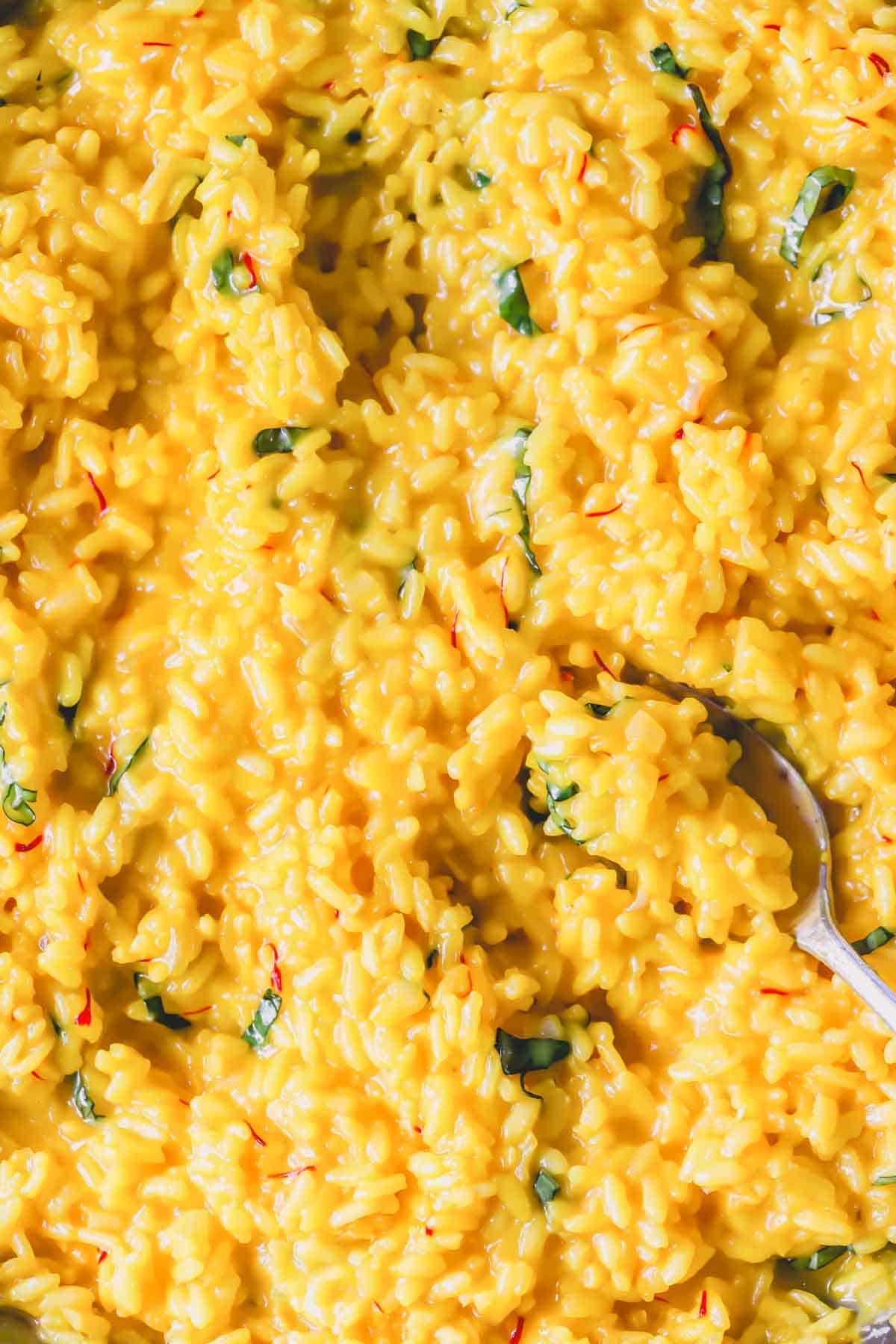 Close view of creamy saffron risotto with a spoon lifting a scoop.