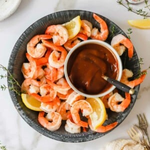 A bowl of cocktail shrimp with cocktail sauce in the center.