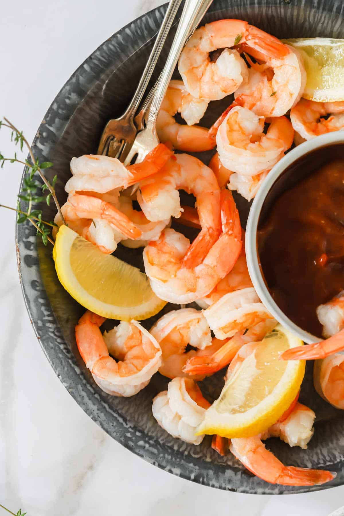 Cocktail shrimp in a bowl with lemon wedges and cocktail sauce.