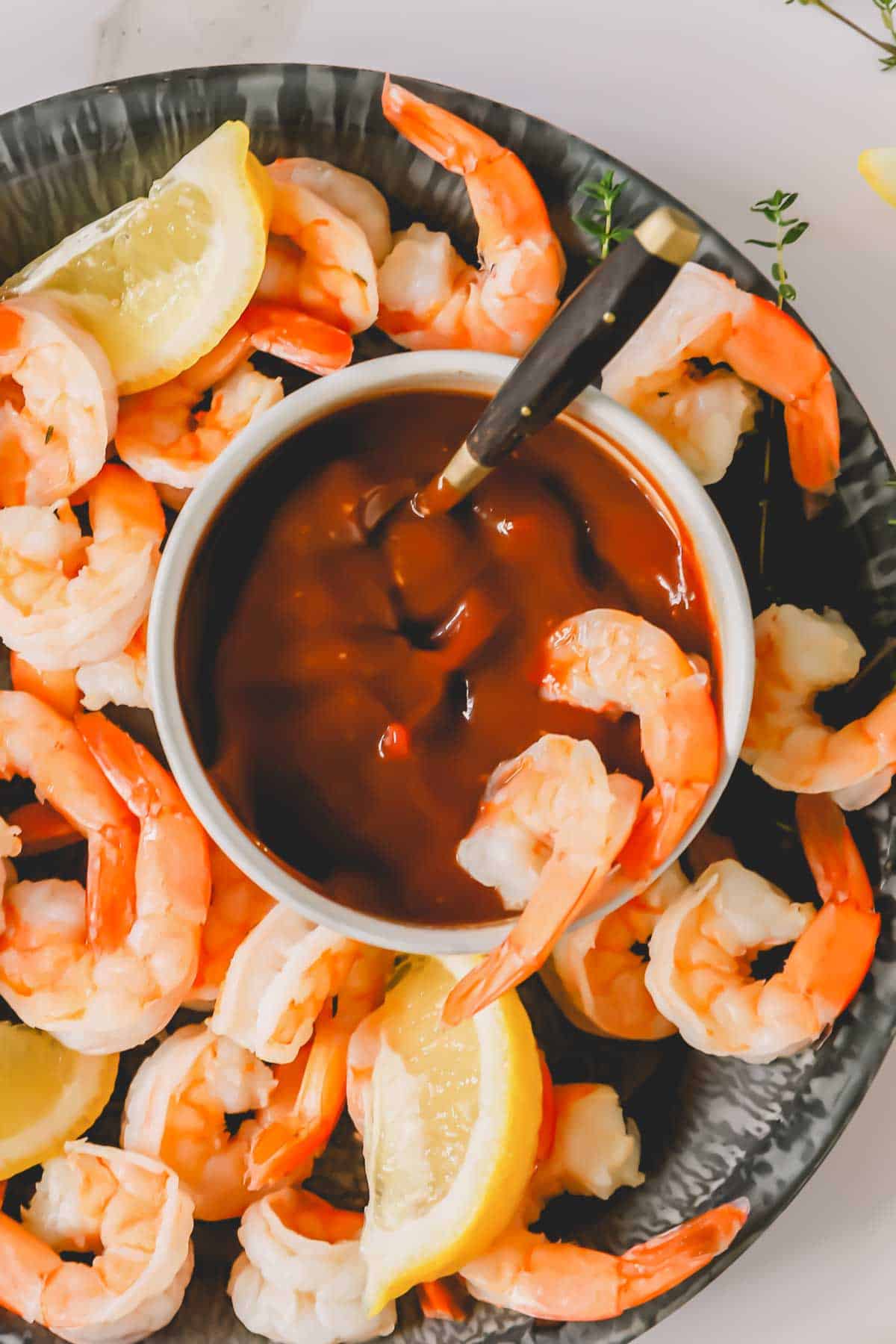 Two shrimp dipped into a bowl of cocktail sauce sitting in a bowl of cocktail shrimp.