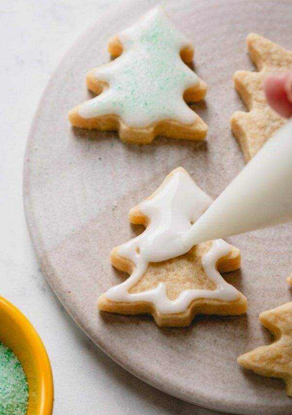 Christmas tree-shaped sugar cookies being flooded with icing.