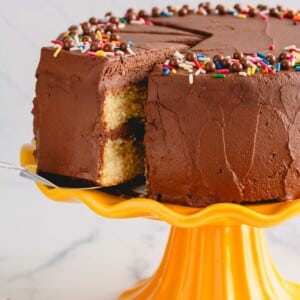 A slice of chocolate frosted yellow cake being lifted from a yellow cake stand.