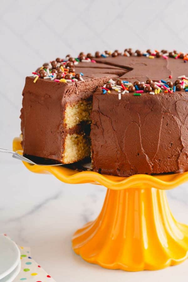 A slice of chocolate frosted yellow cake being lifted from a yellow cake stand.