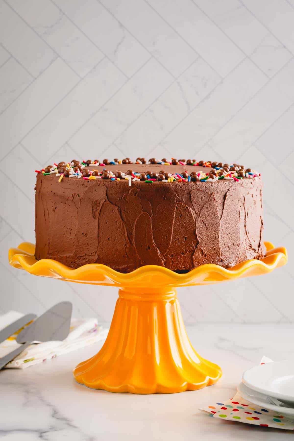 A classic yellow cake with chocolate frosting on a yellow cake stand.