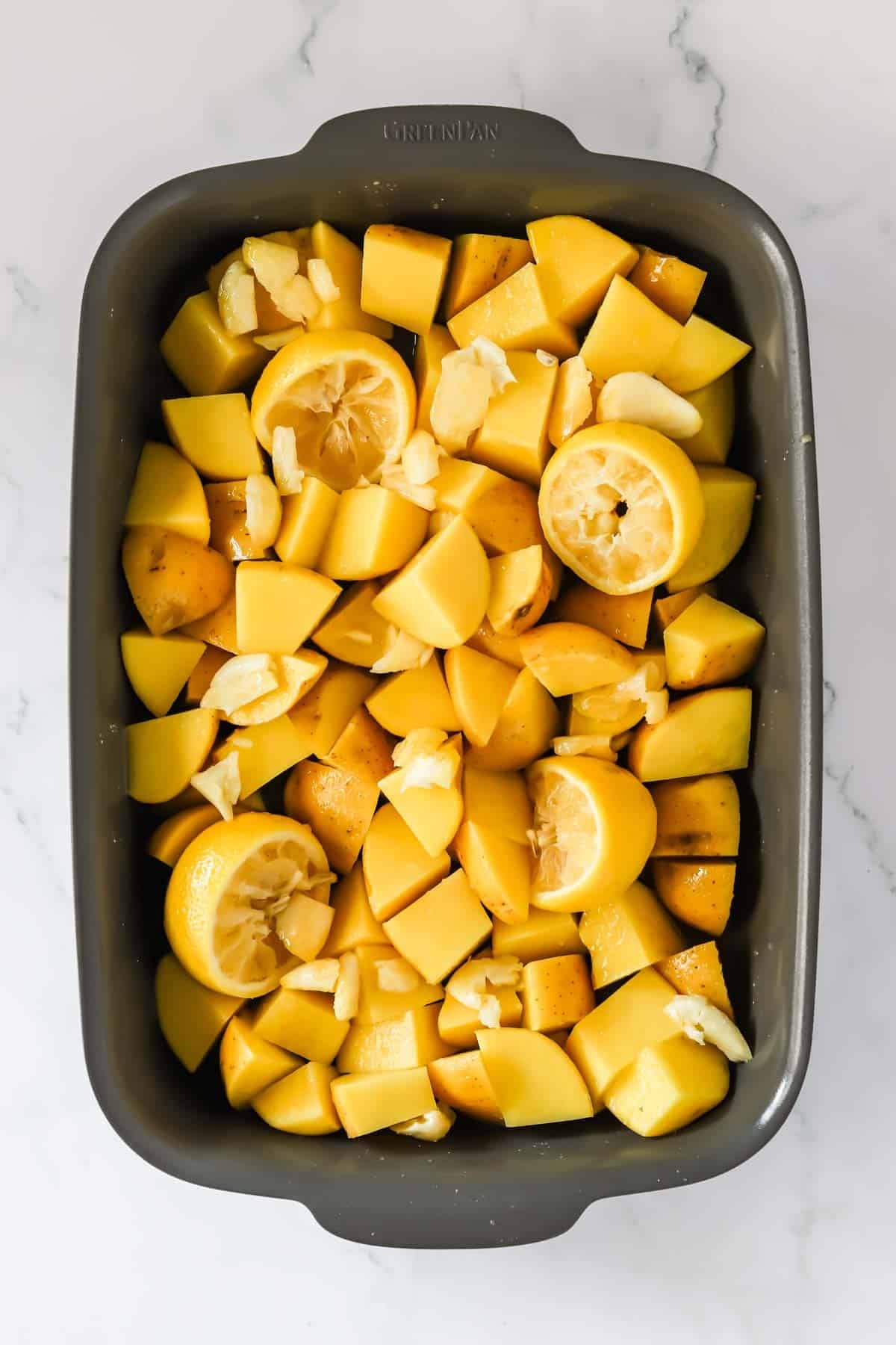A baking dish full of chopped potatoes, smashed garlic, and lemon halves.
