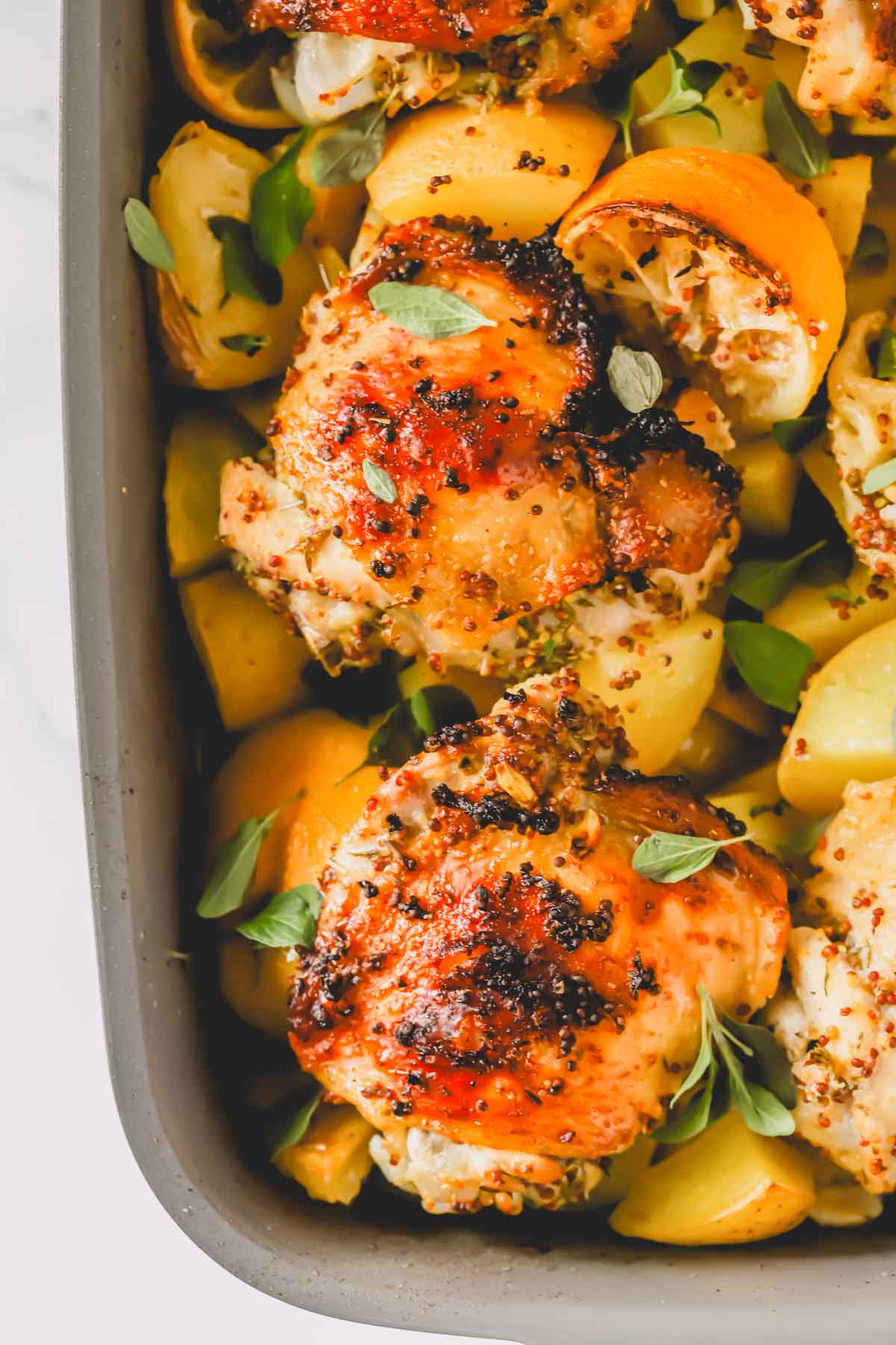 Greek lemon chicken over roasted potatoes in a baking dish with lemon halves.