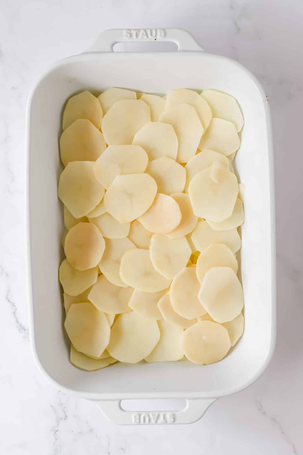 Potato slices arranged in one layer in a white baking dish.