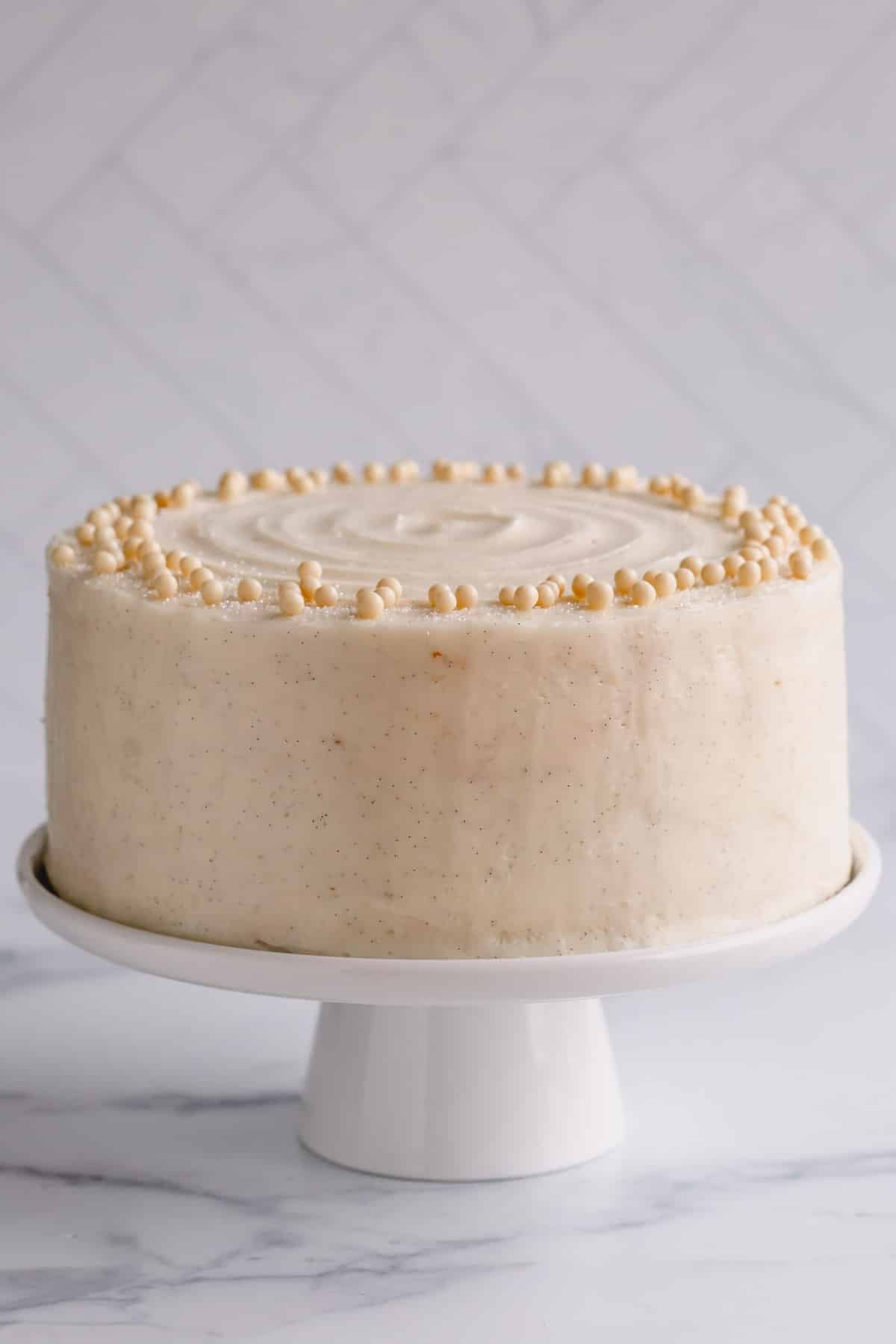 A white cake on a cake stand frosted with vanilla butercream.