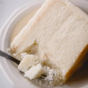 A slice of white cake on a plate with a fork taking a bite.
