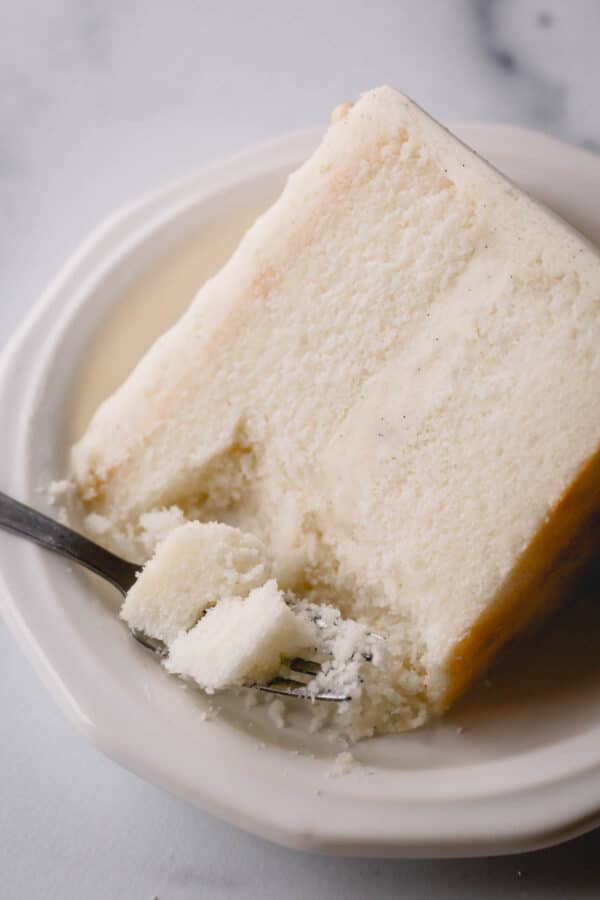 A slice of white cake on a plate with a fork taking a bite.