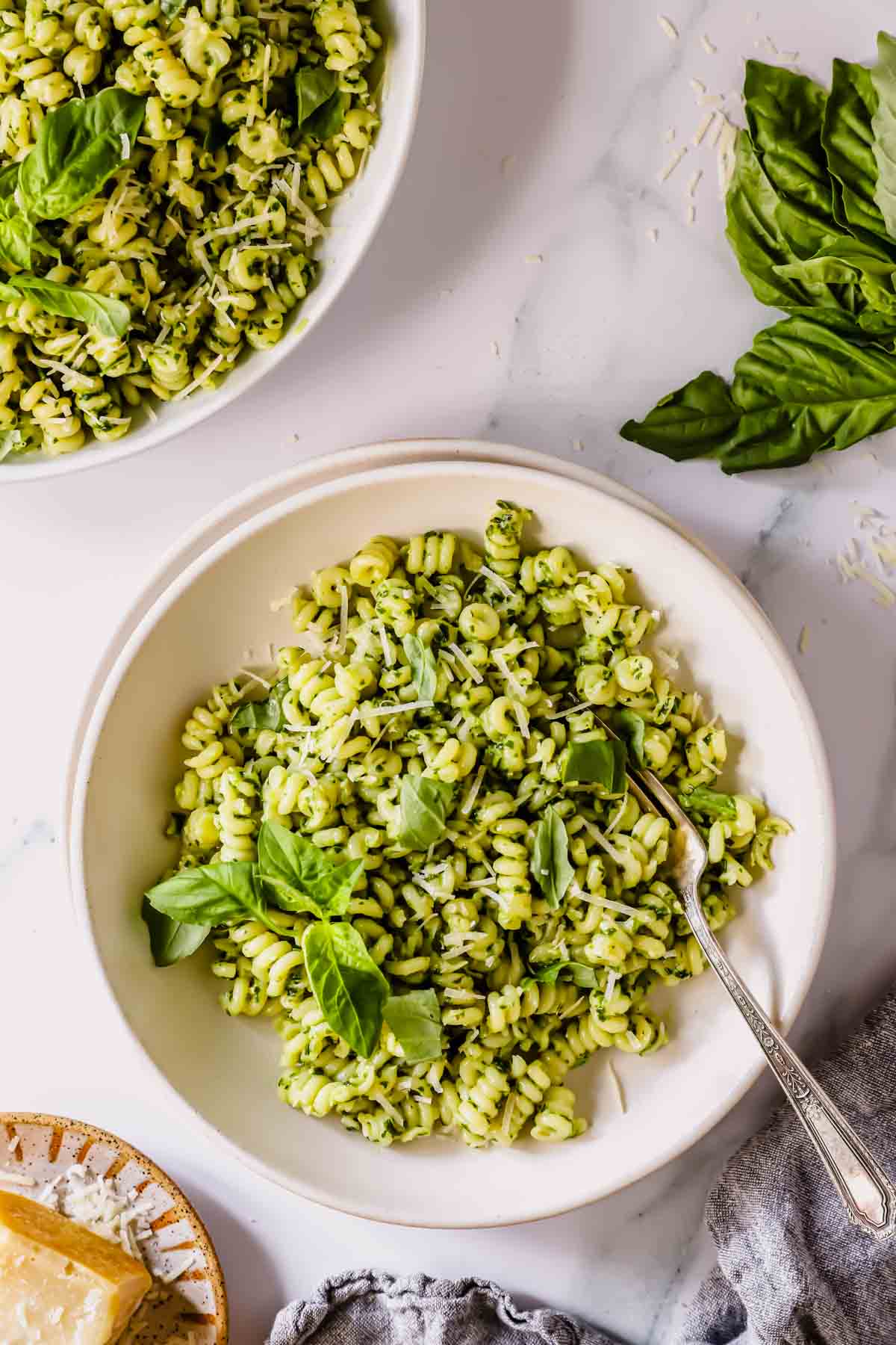 A bowl of basil pesto pasta with a fork and a second bowl of pasta to the side.