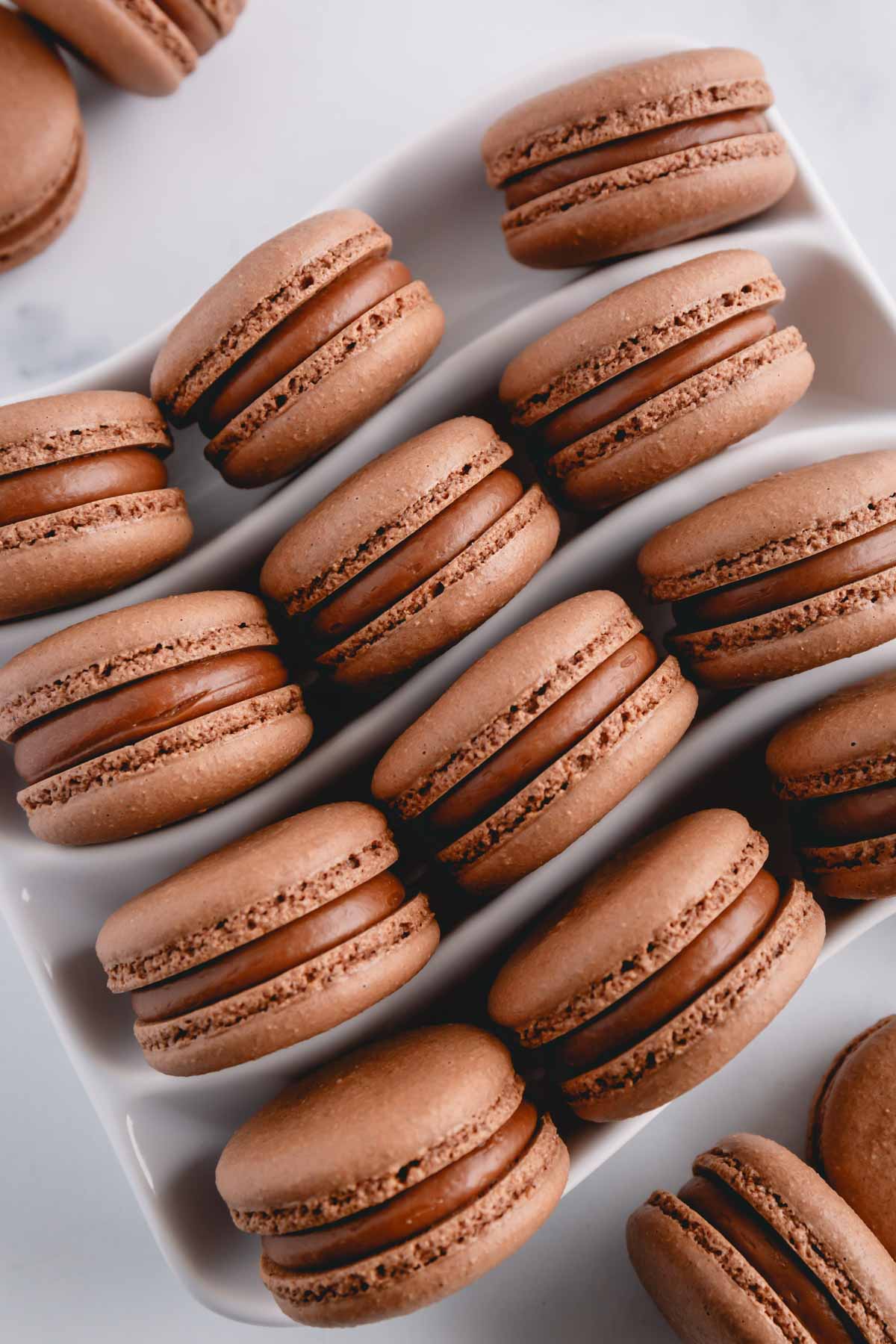 Chocolate macarons filled with chocolate filling in a white serving platter.