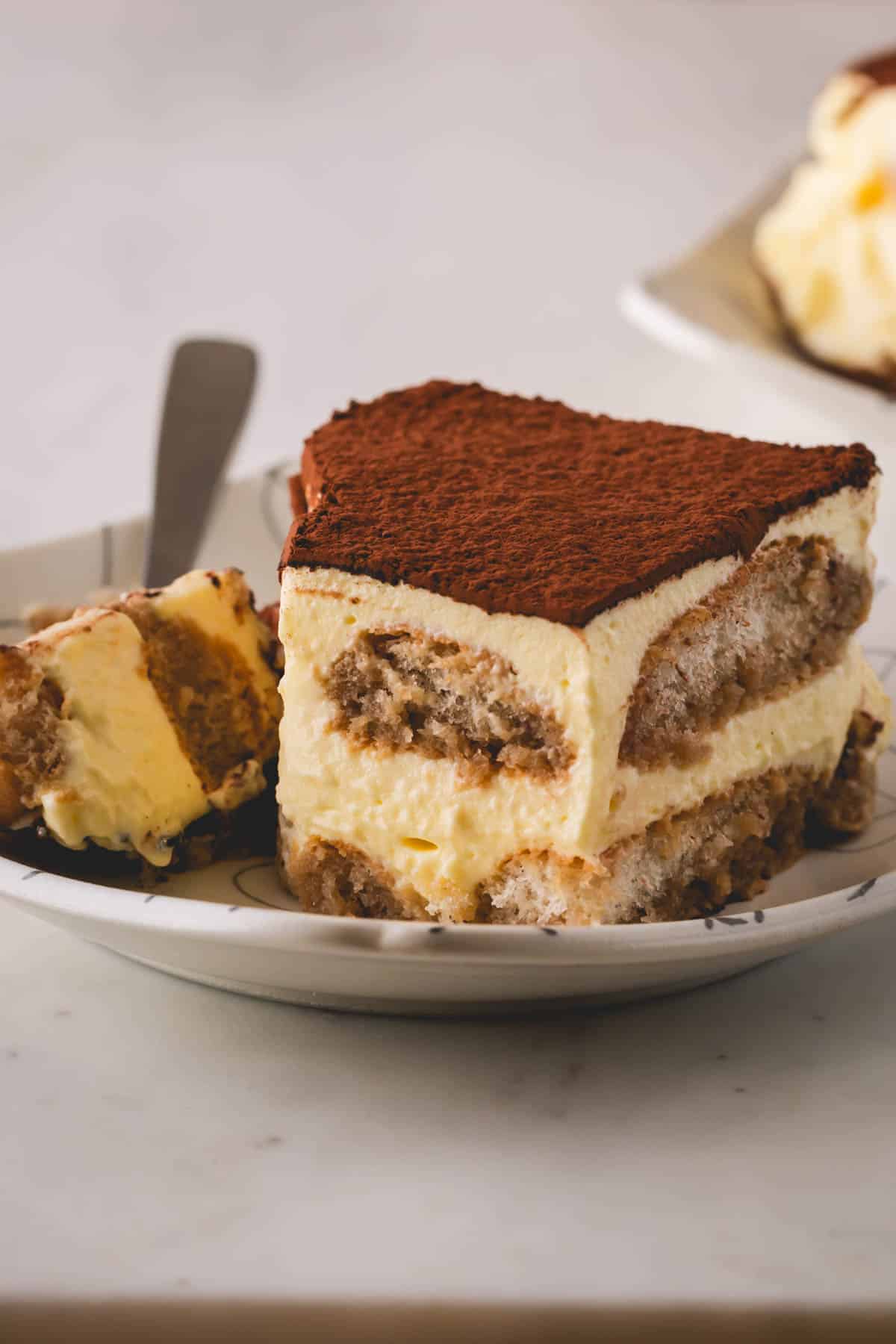 A square of classic tiramisu on a plate with a fork holding the corner bite.