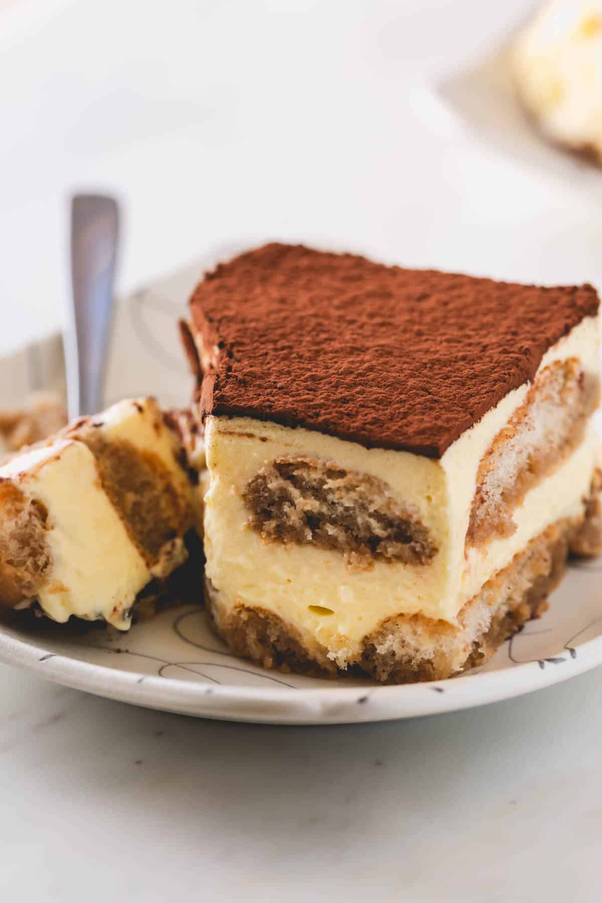 A piece of tiramisu on a plate with a fork holding the corner bite.