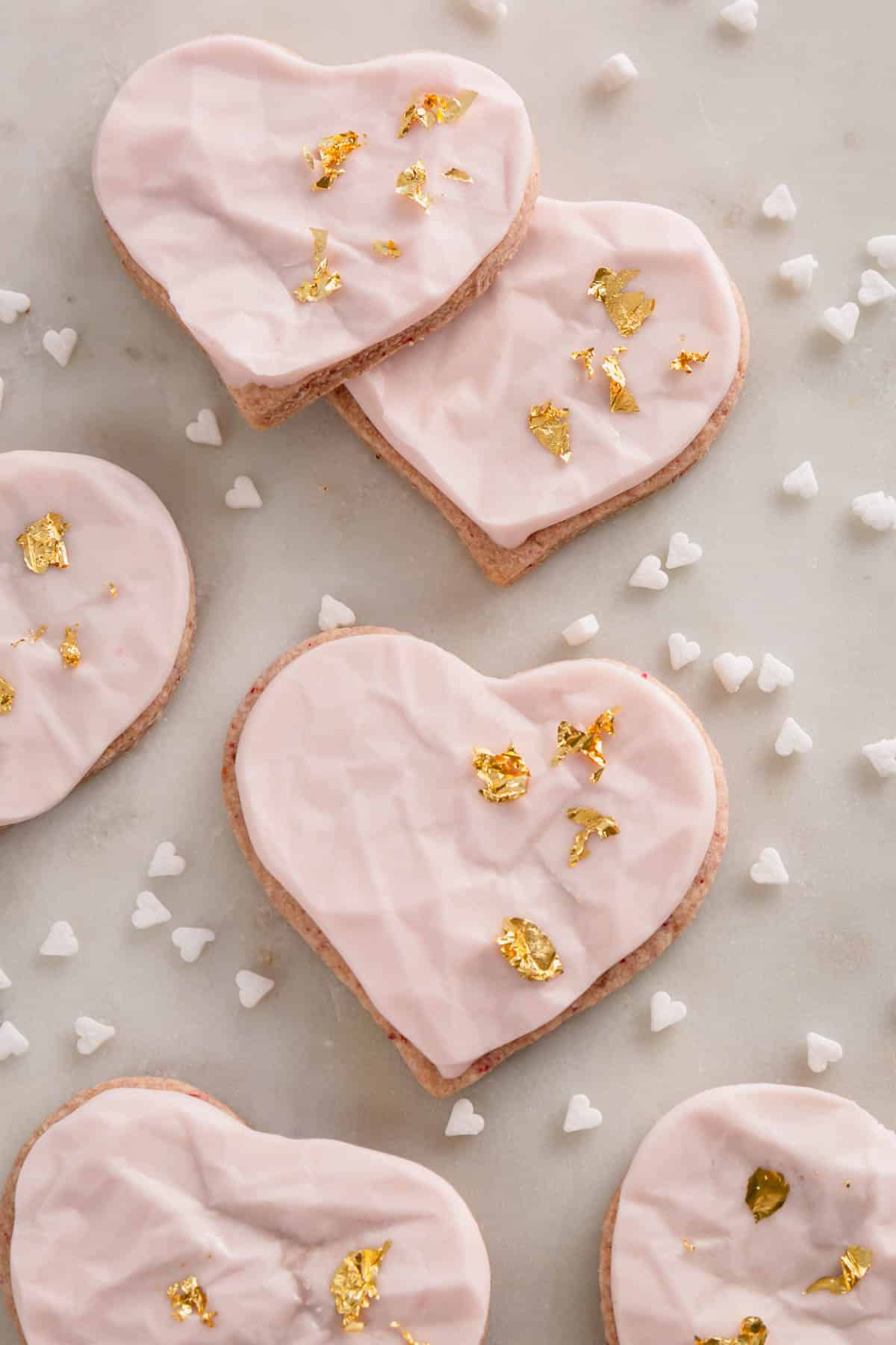 Raspberry heart-shaped sugar cookies with pink icing and gold leaf decoration.