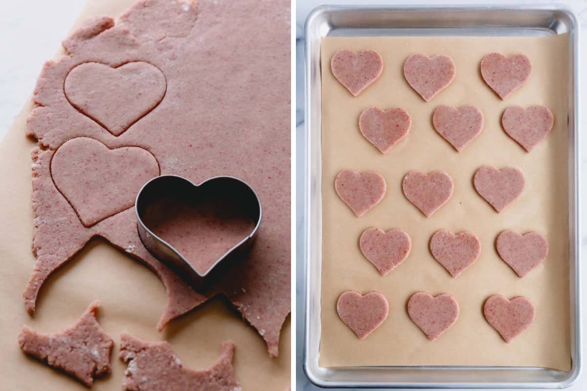 A heart-shaped cookie cutter shaping pink dough and the cut-out cookies on a lined baking sheet.