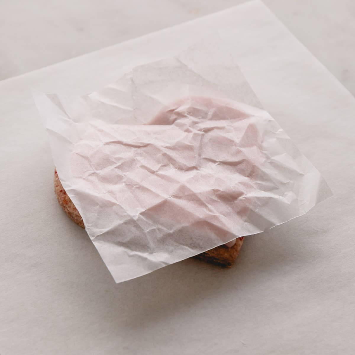 Wax paper being pressed down on top of an iced sugar cookie to create texture.