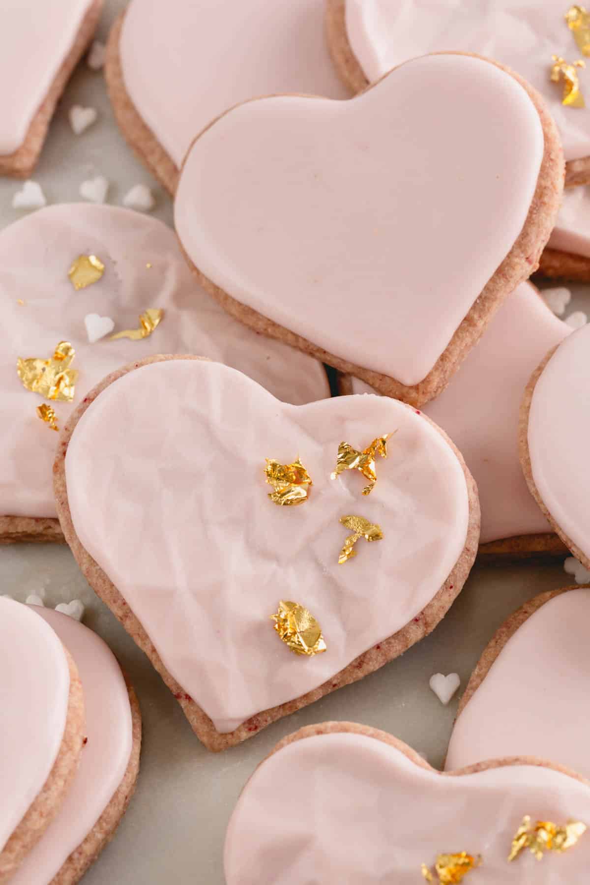 Heart-shaped raspberry sugar cookies with smooth and textured icing and gold leaf decorations.