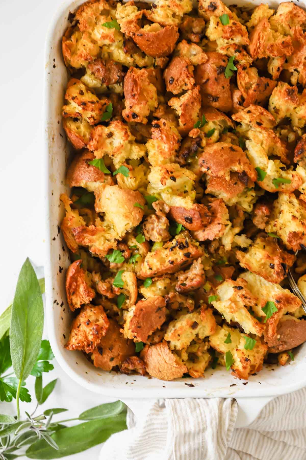 A baking dish full of sausage stuffing topped with fresh herbs.