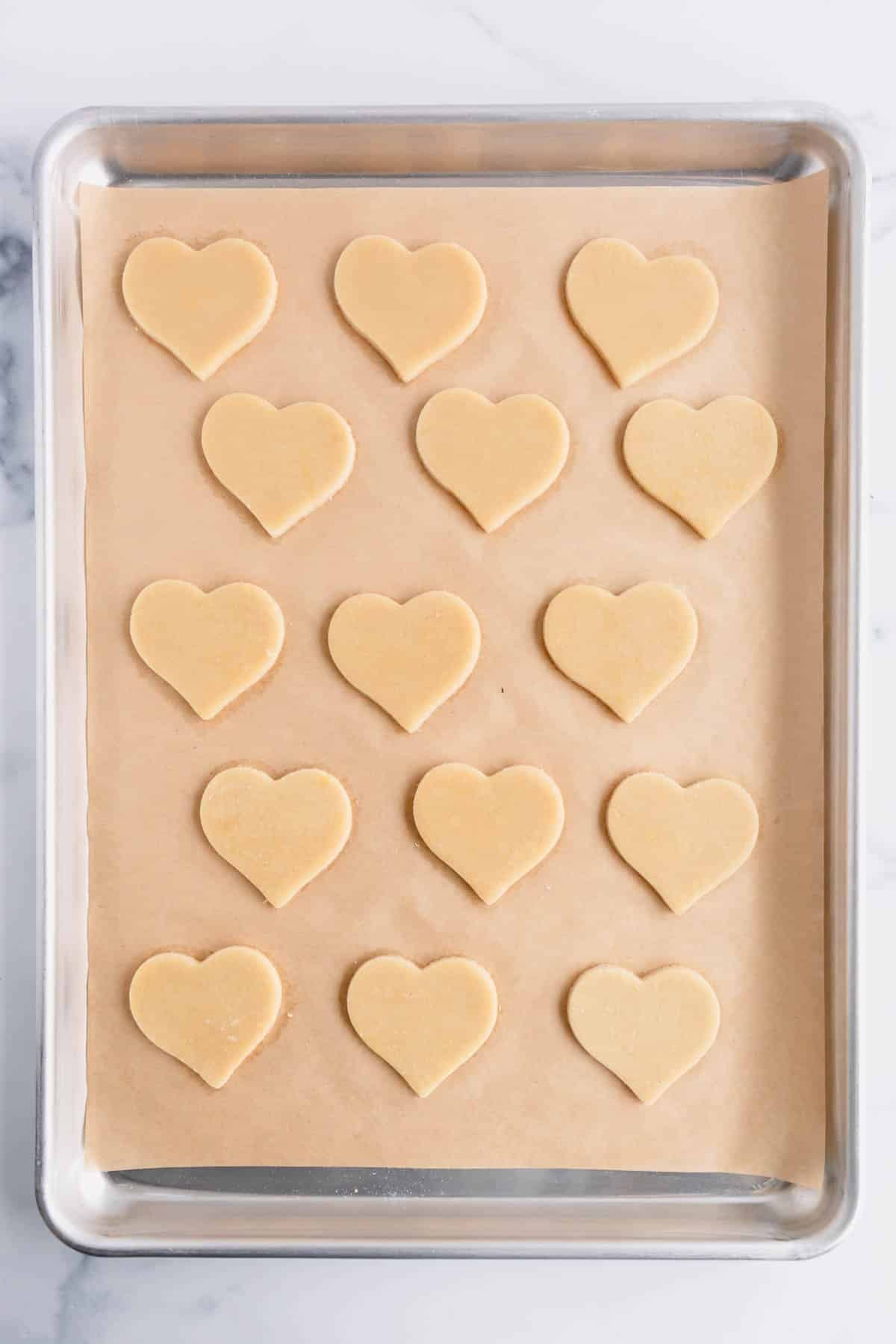 Heart-shaped sugar cookies on a parchment paper lined baking sheet.