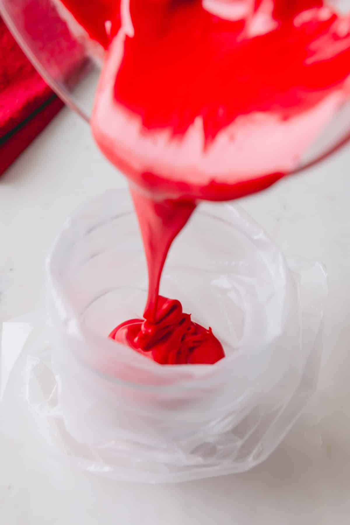 Red royal icing being poured into a piping bag.