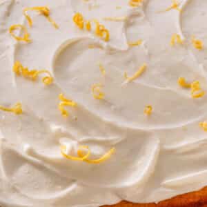 A yellow cake topped with lemon cream cheese frosting and lemon zest curls.
