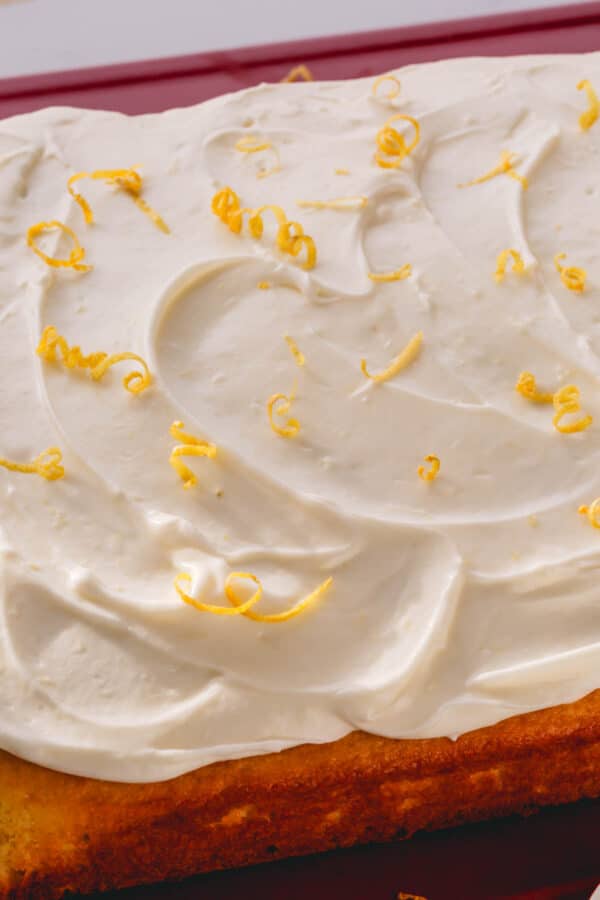 A yellow cake topped with lemon cream cheese frosting and lemon zest curls.