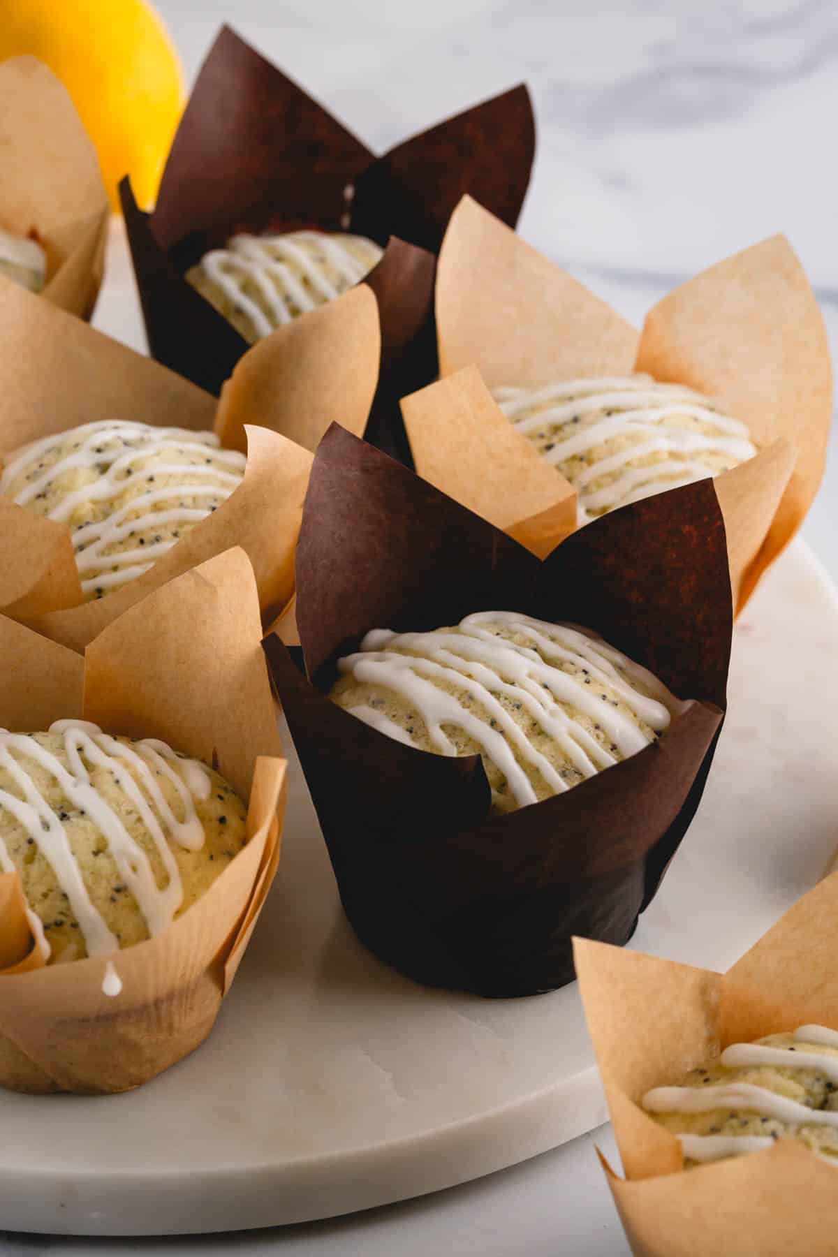 Lemon poppy seed muffins in wrappers topped with a lemon glaze.