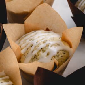 A lemon poppy seed muffin topped with lemon glaze in a paper liner.